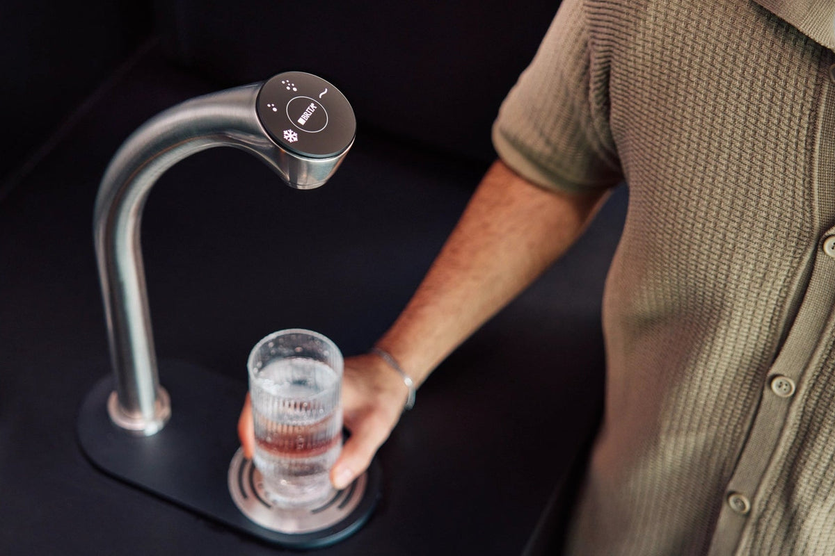 Person grabbing a glass with water from a Extra C-Tap dispenser