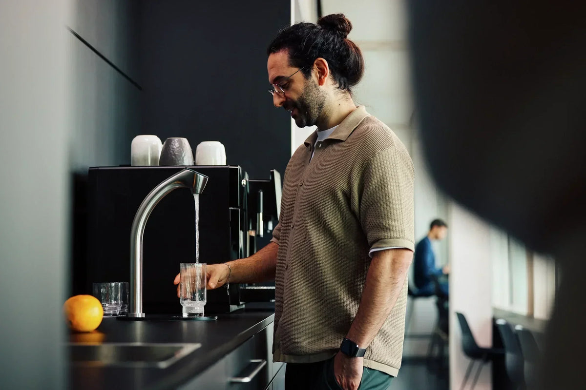 Un homme se tient dans une cuisine et remplit un verre d’eau au robinet.