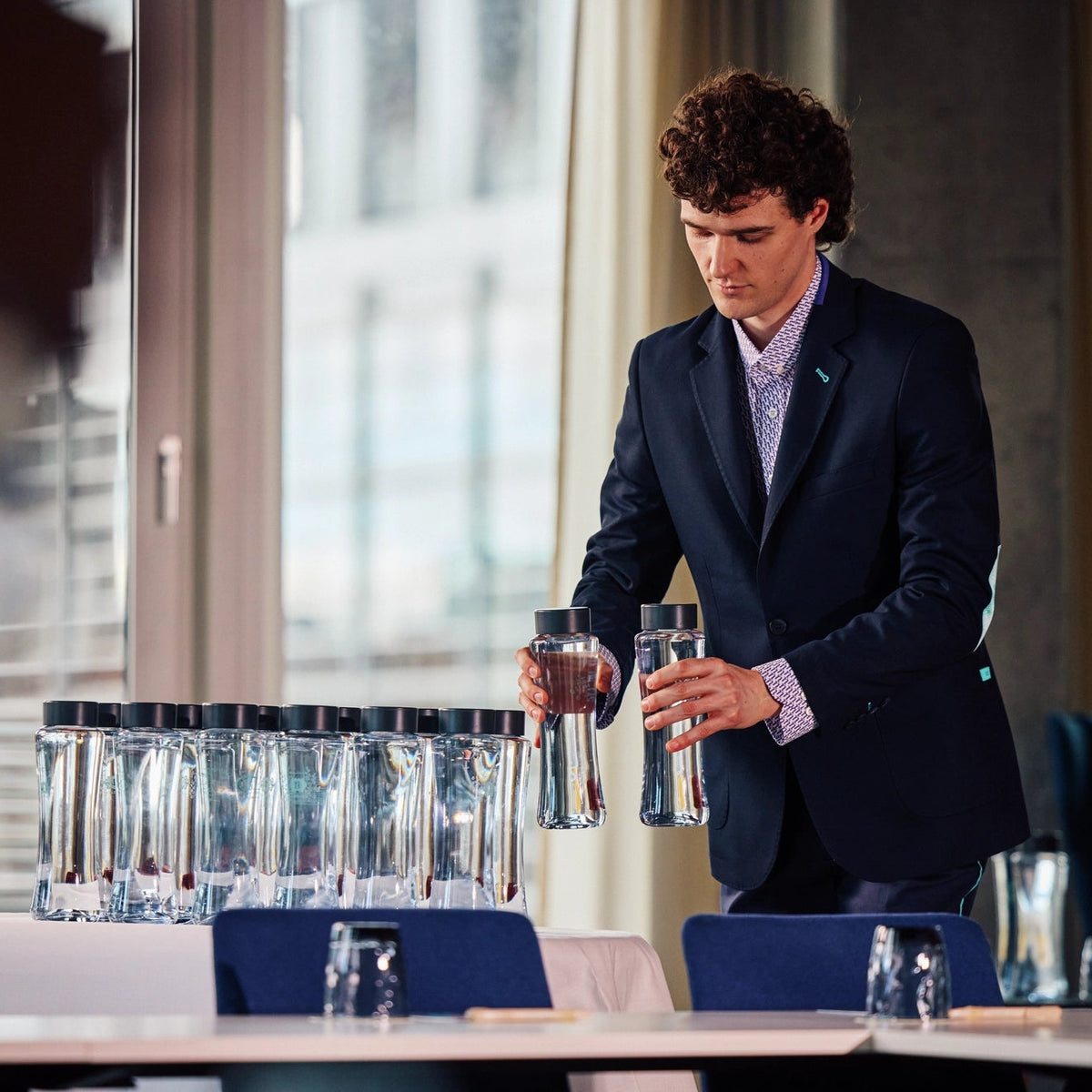 Waiter in a suit holding water bottles, while preparing a meeting table.