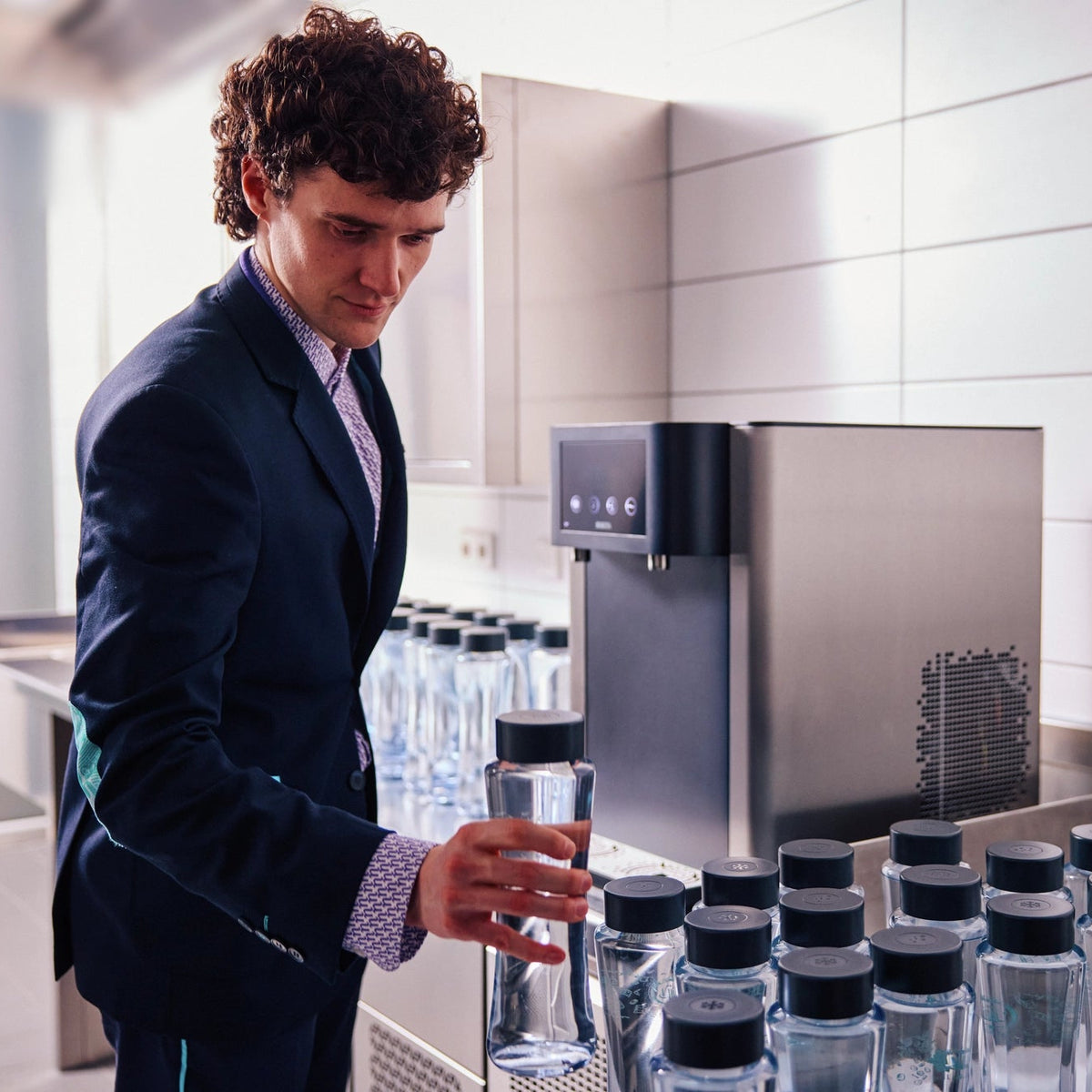 Man in a suit standing in front of a BRITA Fill Pro water dispenser with multiple Twist bottles.
